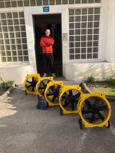 Technicien devant l’entrée d’un immeuble, à côté de quatre brasseurs d’air jaunes prêts à être installés